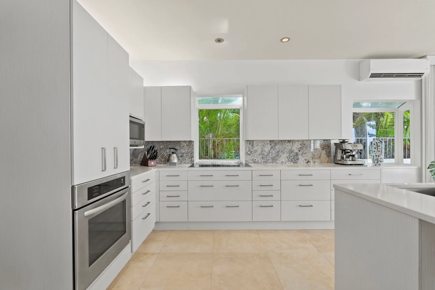 A bright kitchen with white cabinets, a cooking range, and large windows.