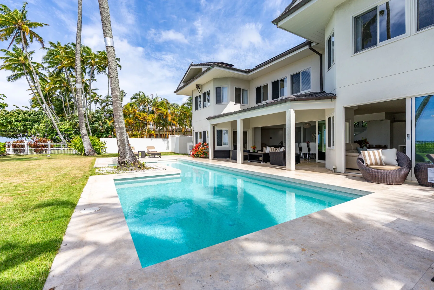 A swimming pool beside a white multi-story house and covered patio.