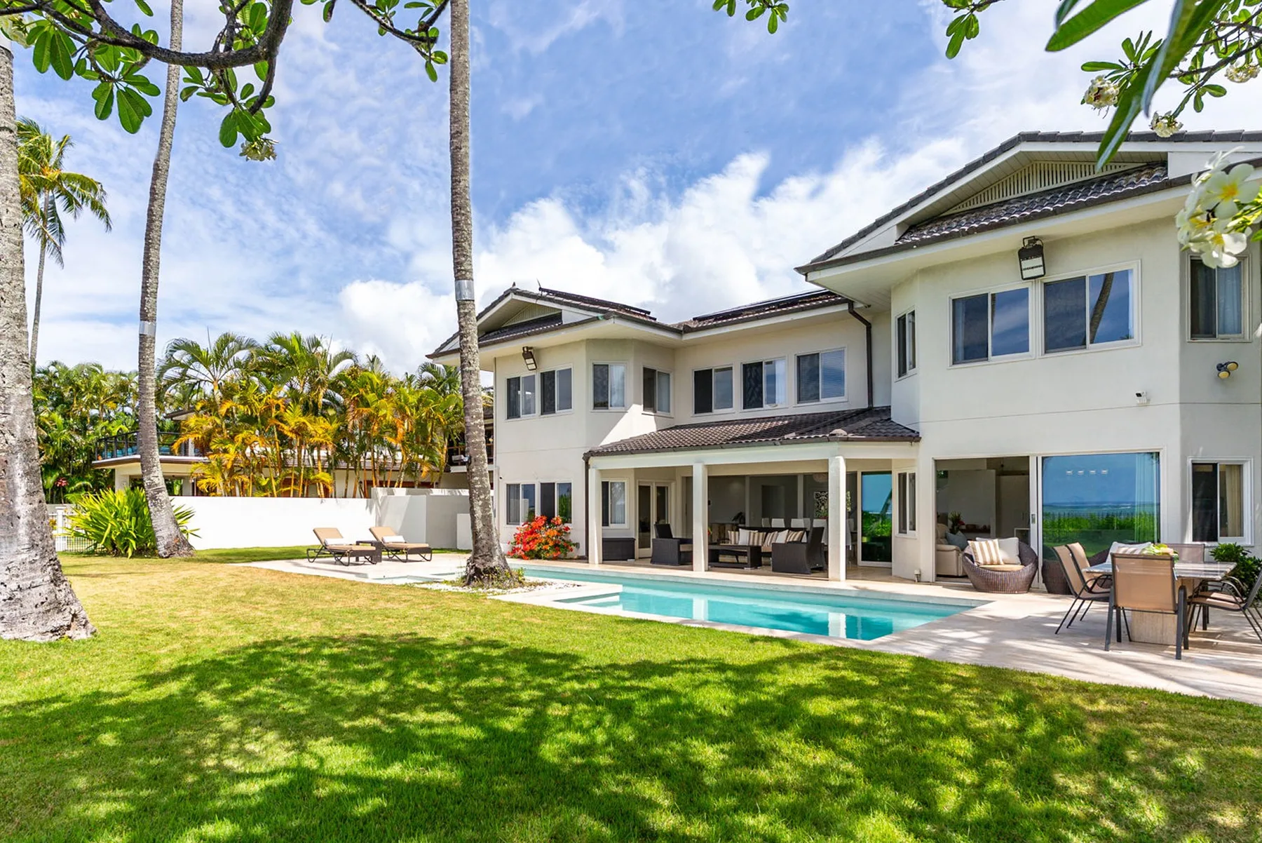 A large house overlooks a lawn, patio seating, and a swimming pool.