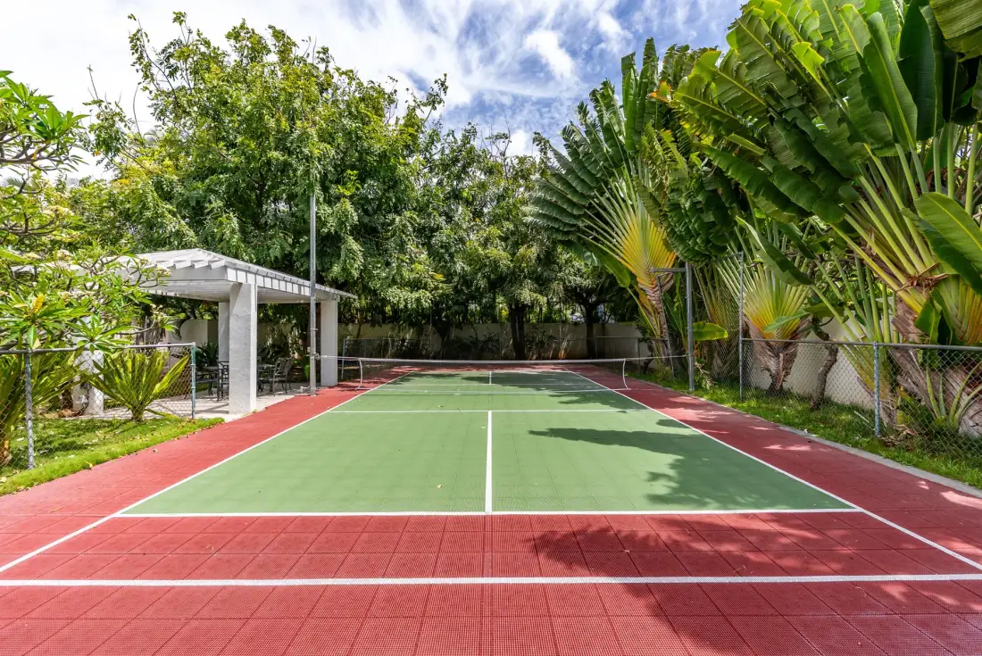 Una cancha de tenis al aire libre está rodeada de vegetación tropical.