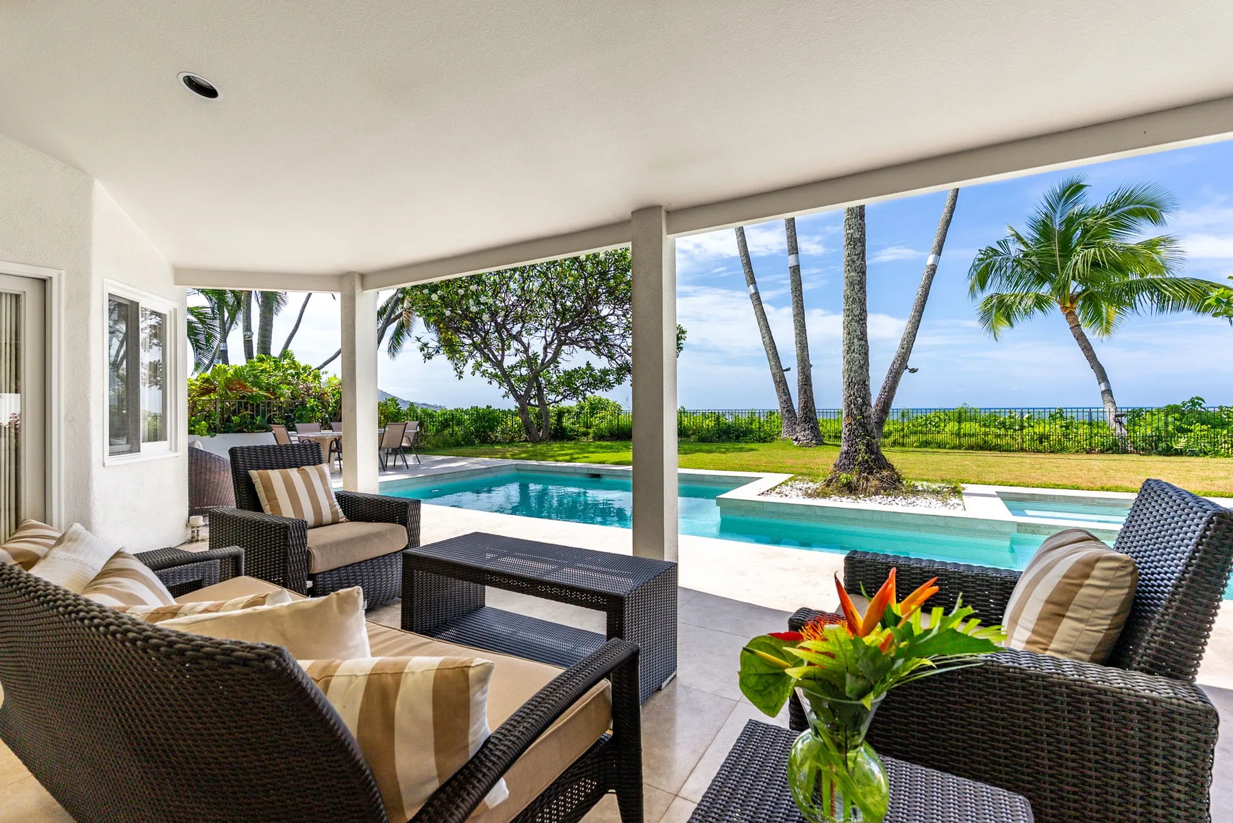 A covered outdoor seating area overlooks a swimming pool and tropical greenery.