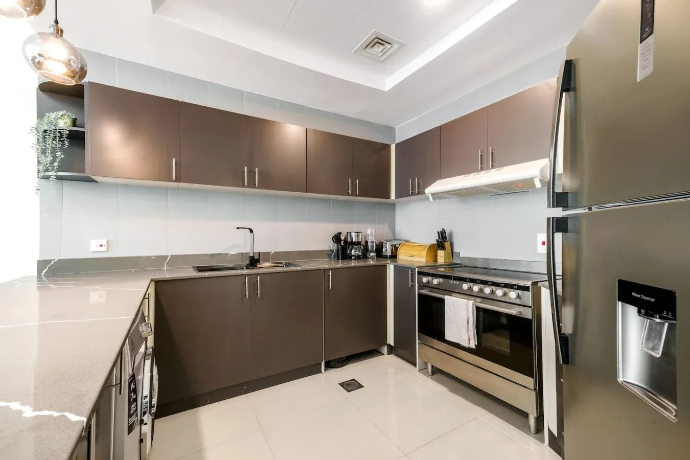 A modern kitchen with dark cabinets, countertop appliances, and a stainless-steel refrigerator.