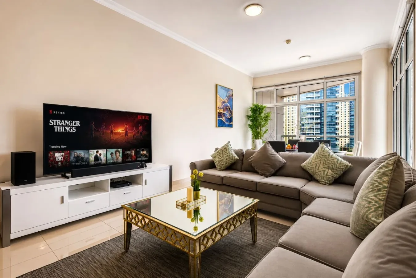 A bright living room with sectional seating, a television, and large windows.