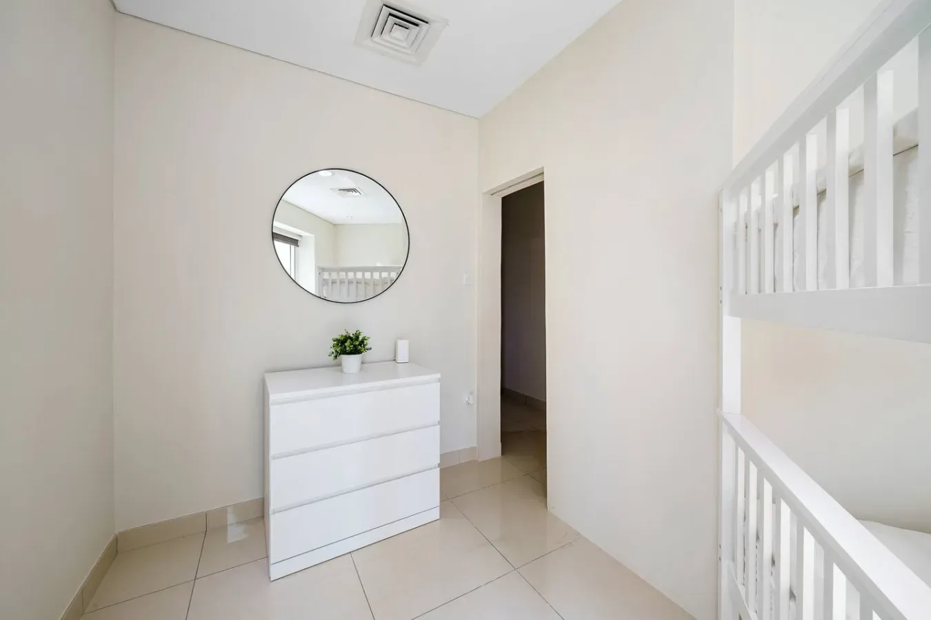 A bright hallway with a white dresser, round mirror, and open doorway.
