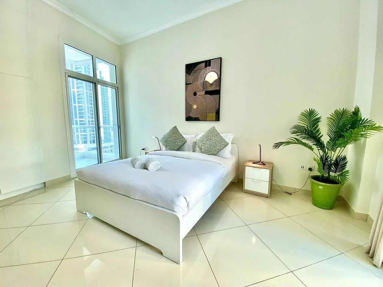 A bright bedroom with a bed, tall windows, and a potted plant.