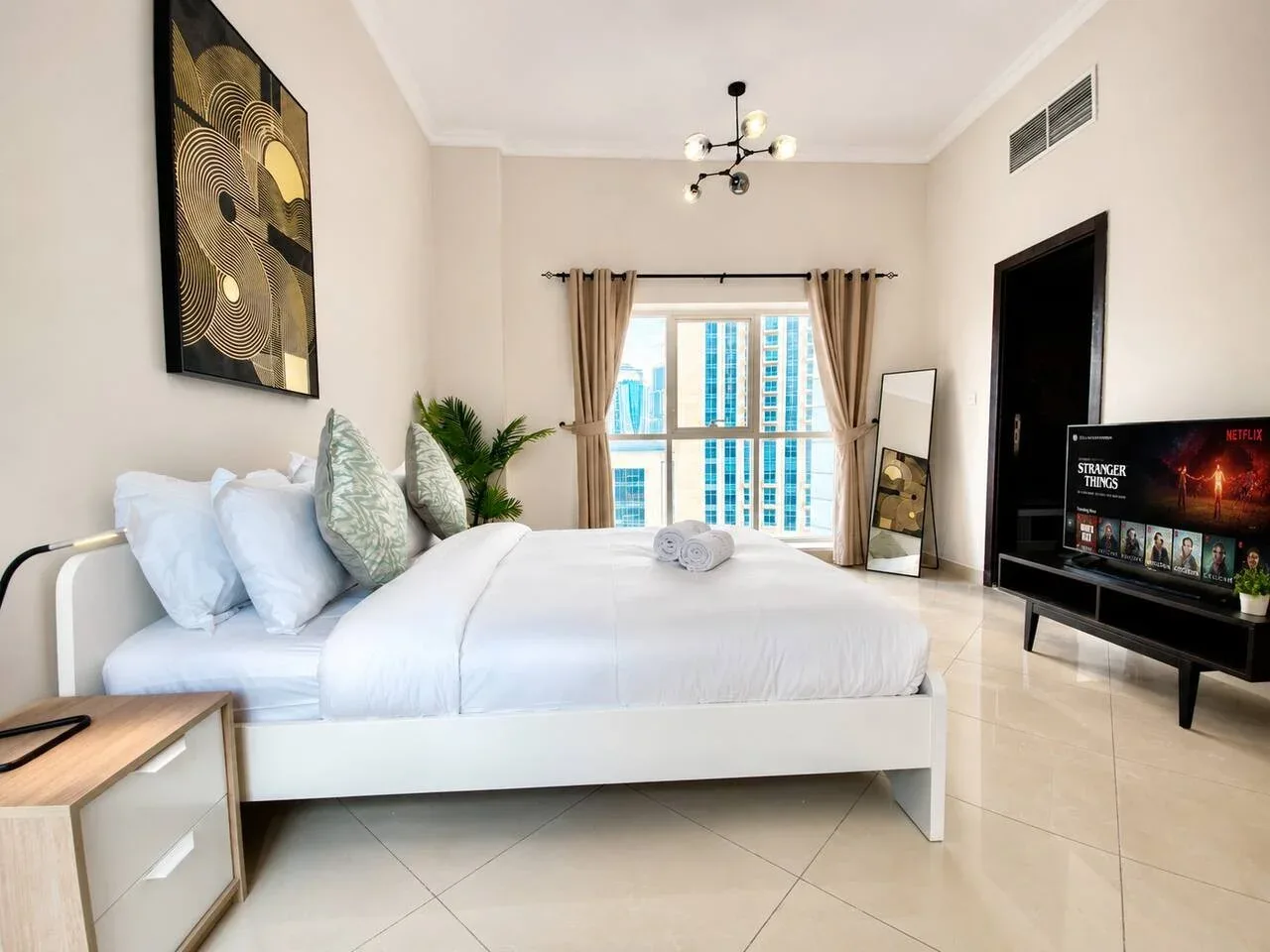 A bright bedroom features a neatly made bed and large windows with curtains.