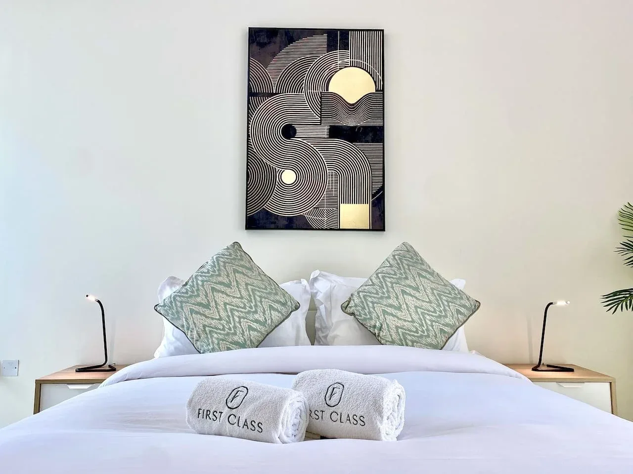 A neatly made bedroom bed with patterned cushions and framed artwork above the headboard.