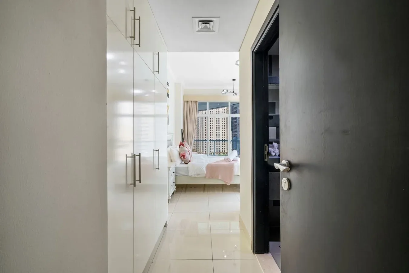 A bedroom is visible through a hallway lined with built-in cabinets.