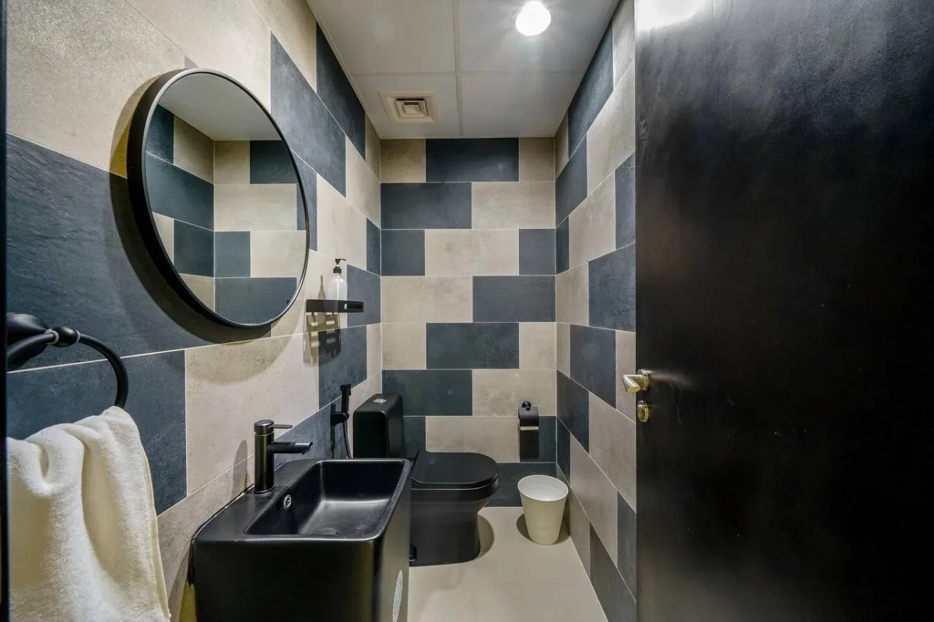 A tiled bathroom with a sink, toilet, and round wall mirror.