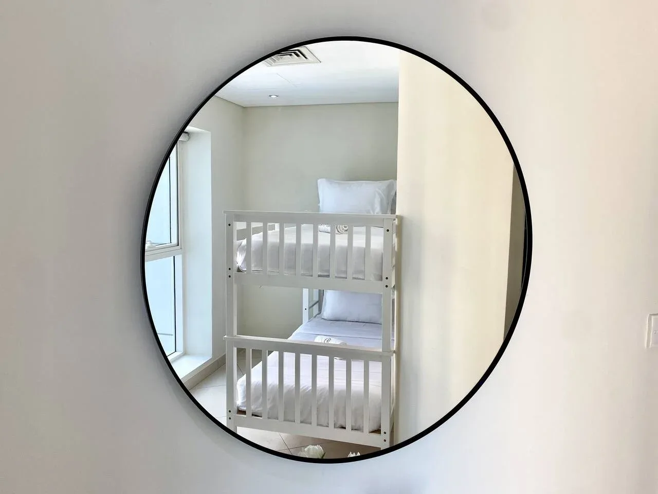 A nursery with a white bunk bed beside a tall window.