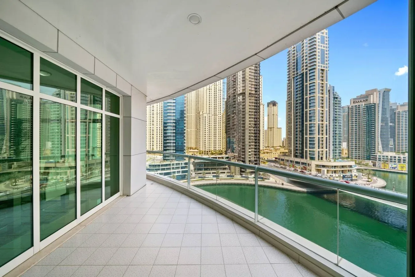 A tiled balcony with glass railings overlooks a cluster of high-rise buildings.