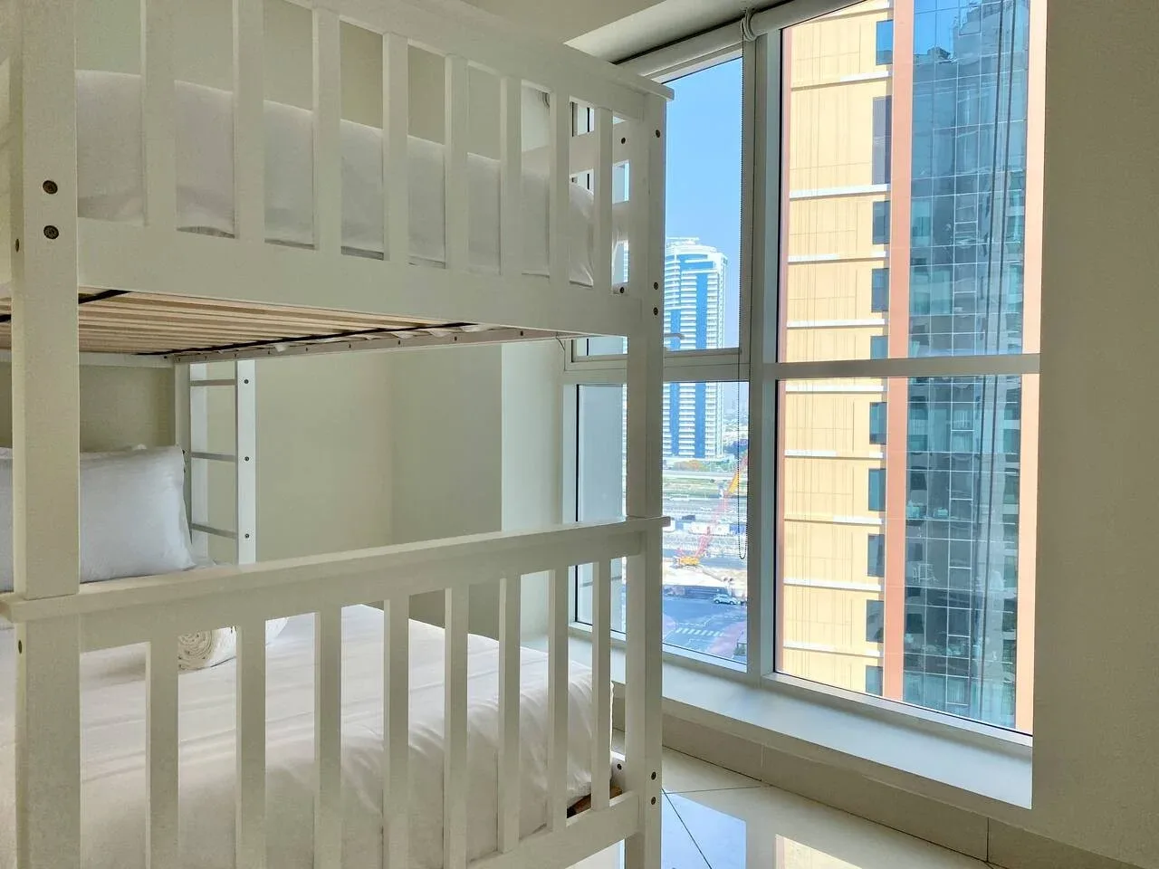 A bunk bed stands beside large windows overlooking nearby buildings.