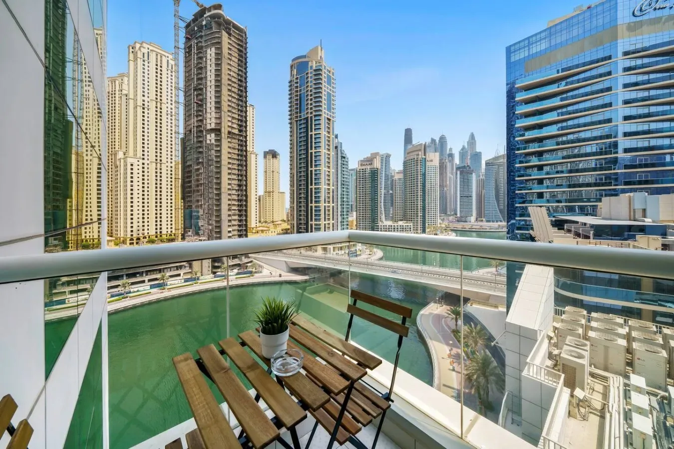 A balcony seating area overlooks a city skyline, with a small table and potted plant.