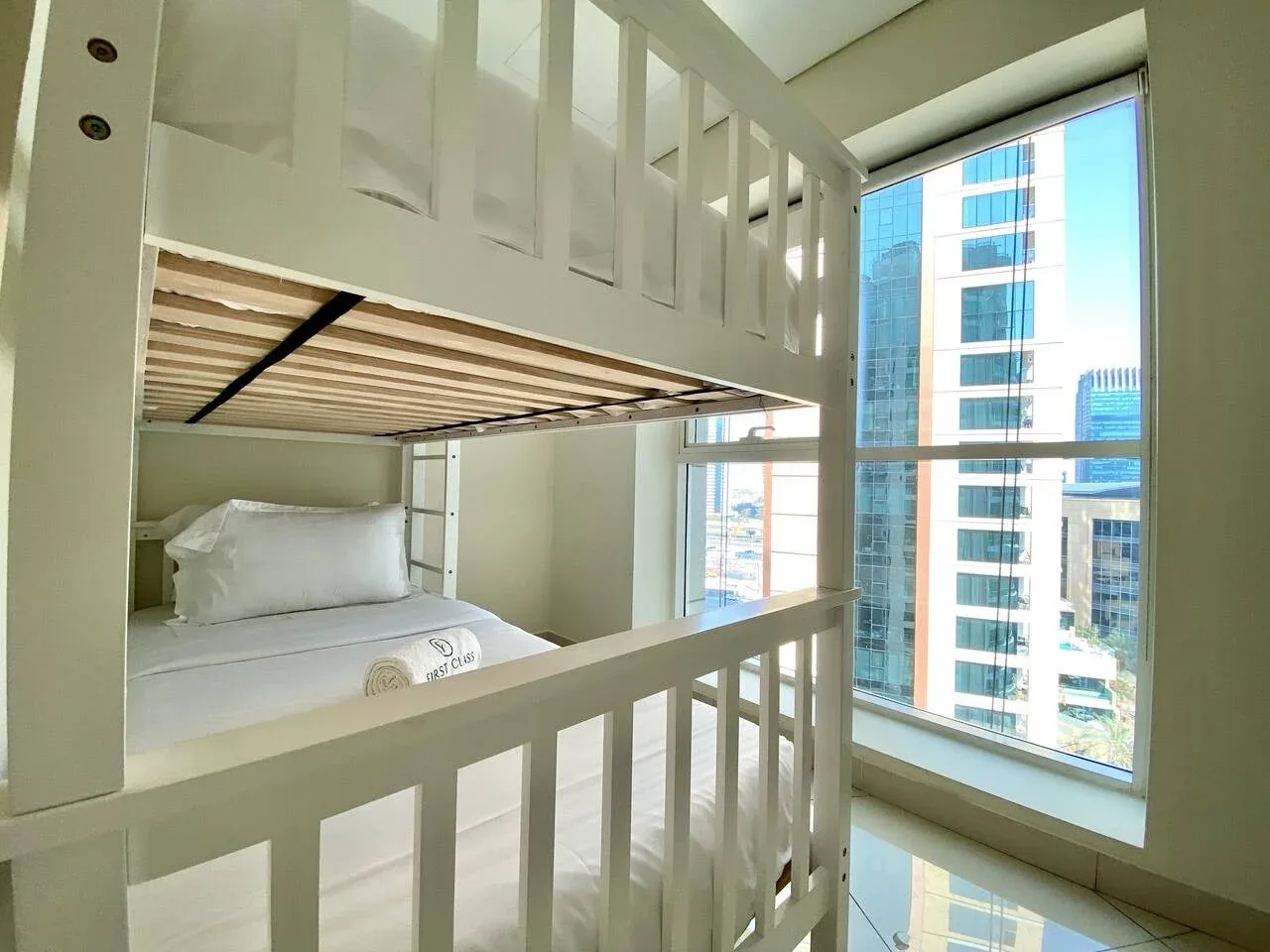 A bunk bed sits beside a large window overlooking nearby buildings.