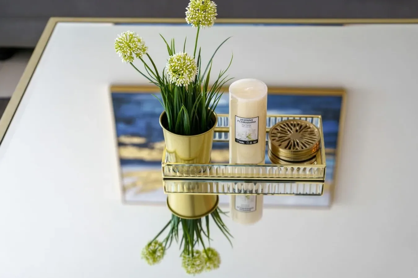 A gold tray with a potted plant, candle, and small round container rests on a table.