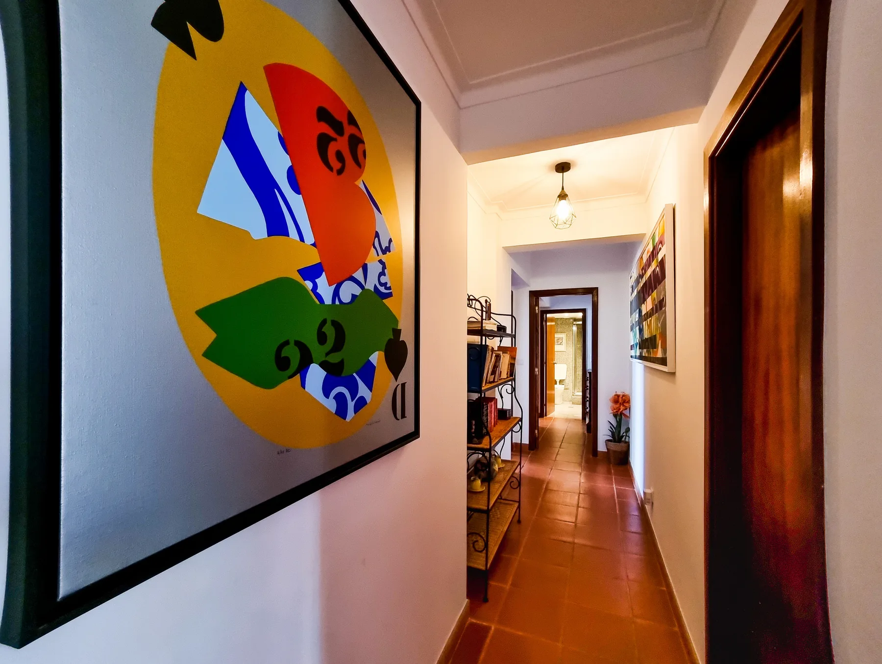 A narrow hallway with framed artwork and a tiled floor.