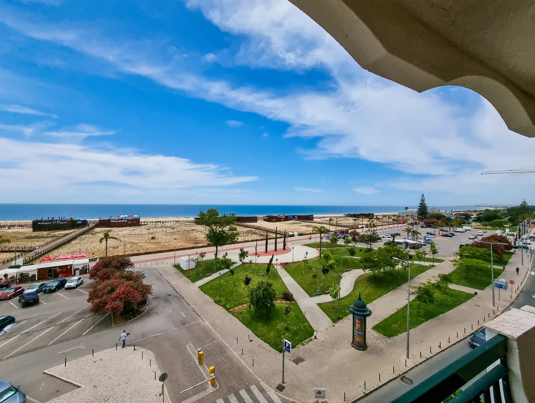 View from a balcony overlooking a landscaped park, roads, and the sea.