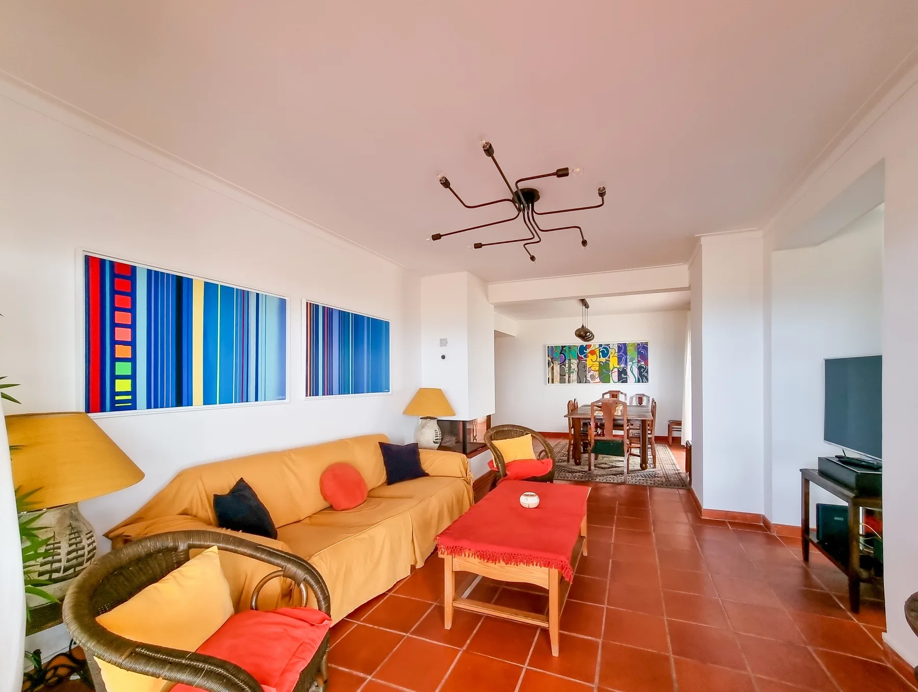 A living room with seating and a red coffee table, opening onto a dining area.