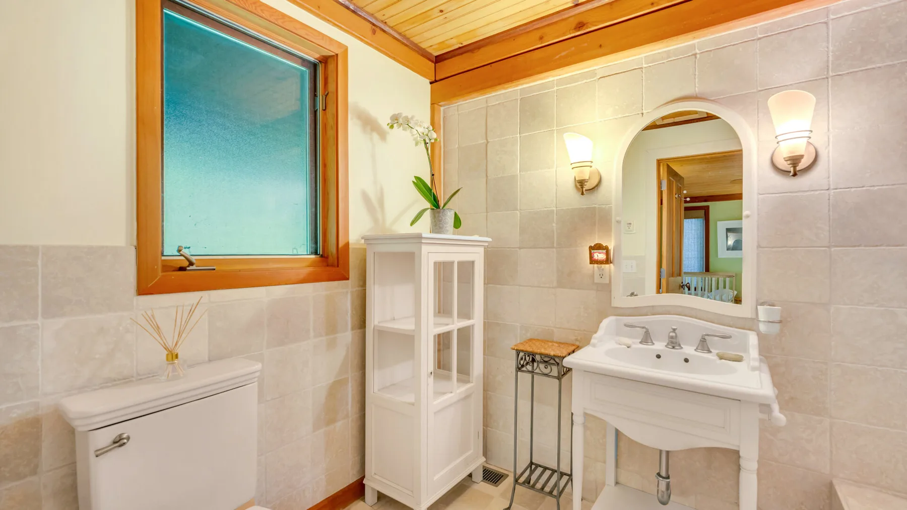 Un baño alicatado con un lavabo bajo un espejo arqueado y una ventana grande.
