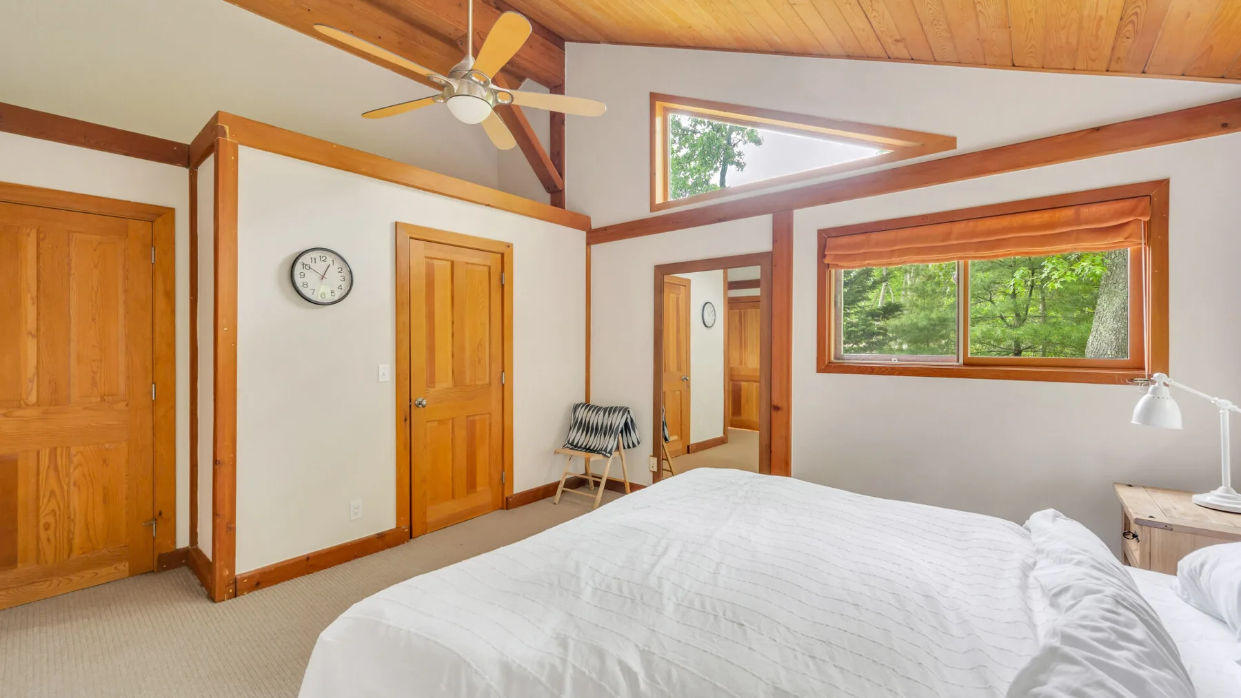 Un dormitorio con una cama, ventanas con marcos de madera y un ventilador de techo.