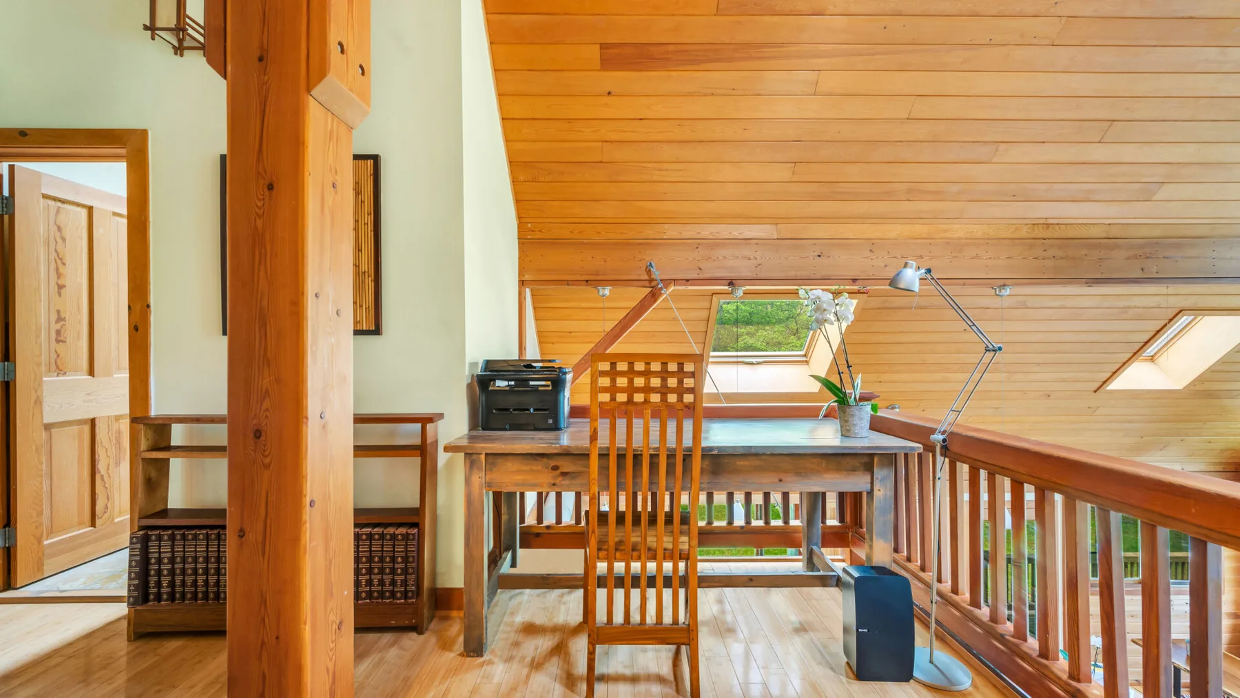 Un espacio de trabajo en un altillo revestido de madera, con escritorio, silla y tragaluz.