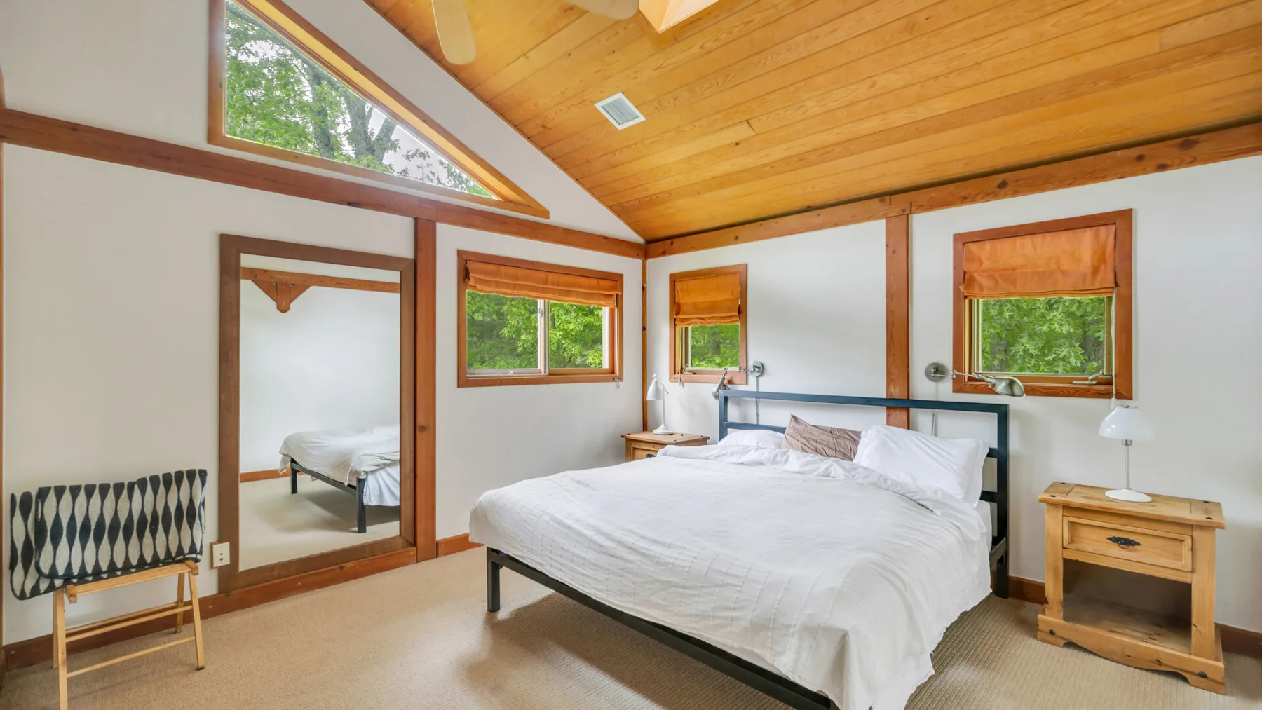 Un dormitorio con una cama grande, techo revestido de madera y ventanas con vistas a la vegetación.