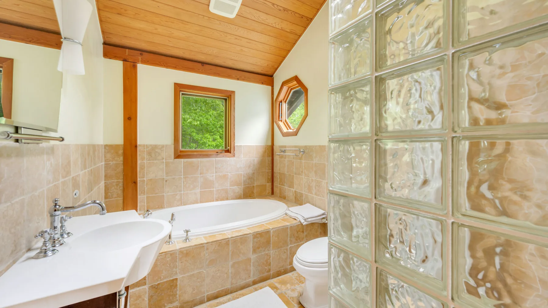 Un baño con bañera, lavabo y una pared divisoria de bloques de vidrio.