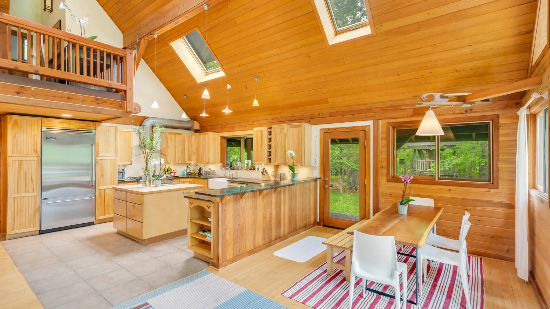 Una luminosa cocina abierta con comedor, paredes revestidas de madera y techo inclinado.