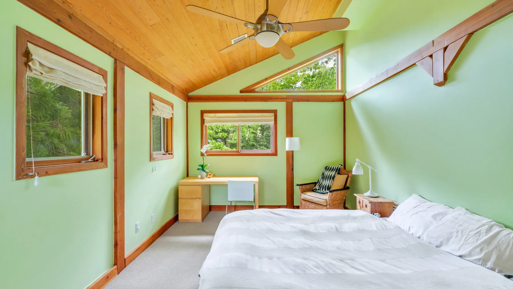 Un dormitorio con cama, escritorio y ventanas bajo un techo inclinado de madera.