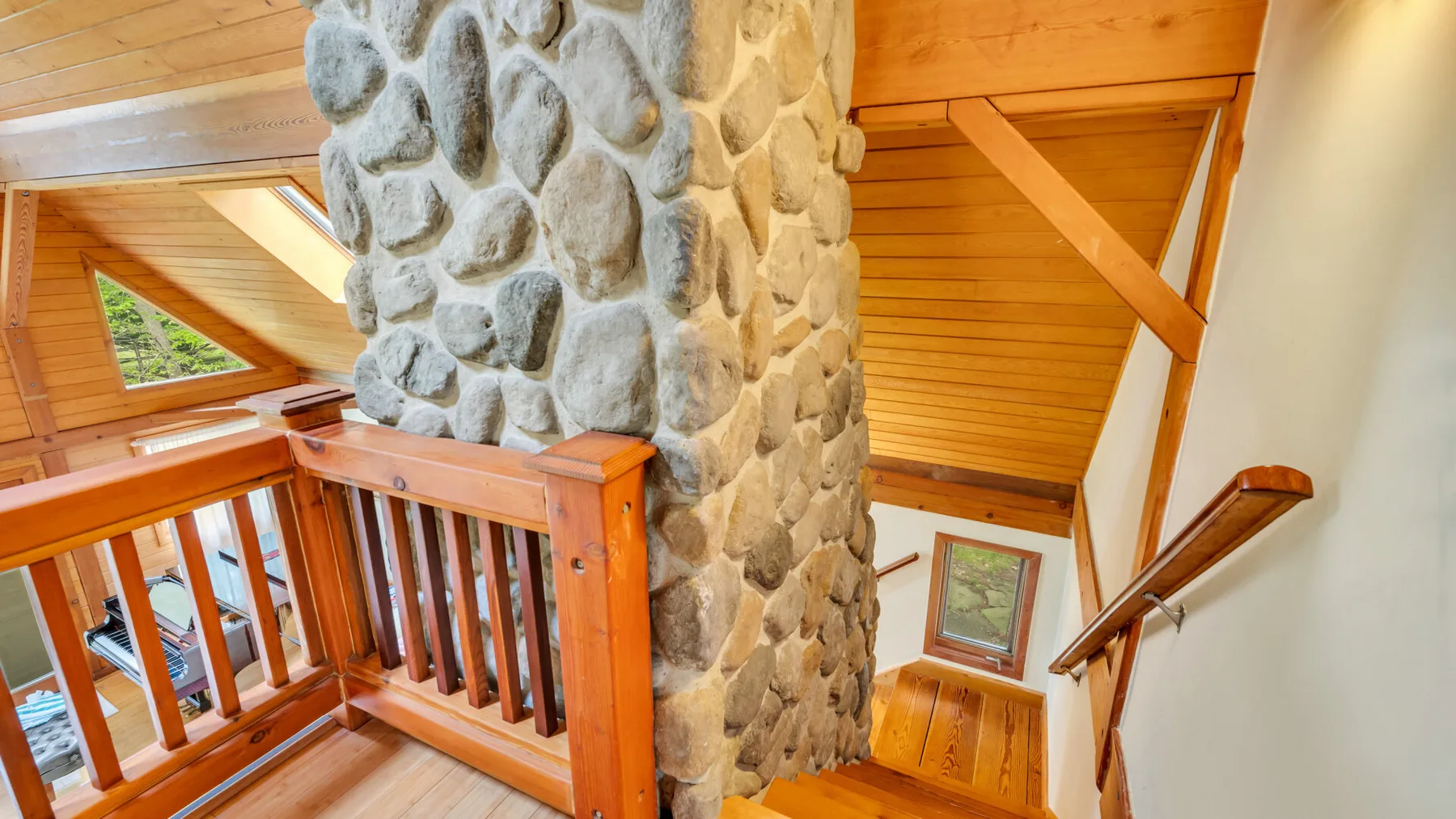 Una escalera y un balcón de madera rodean una columna de piedra bajo un techo inclinado.