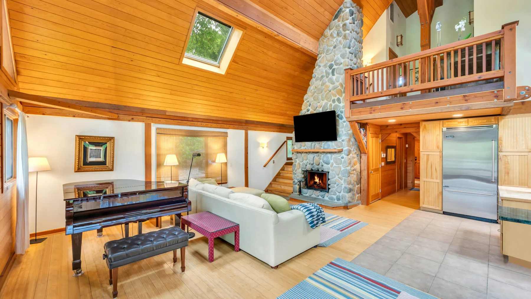 Una sala de estar con techo alto, chimenea de piedra, asientos y piano.