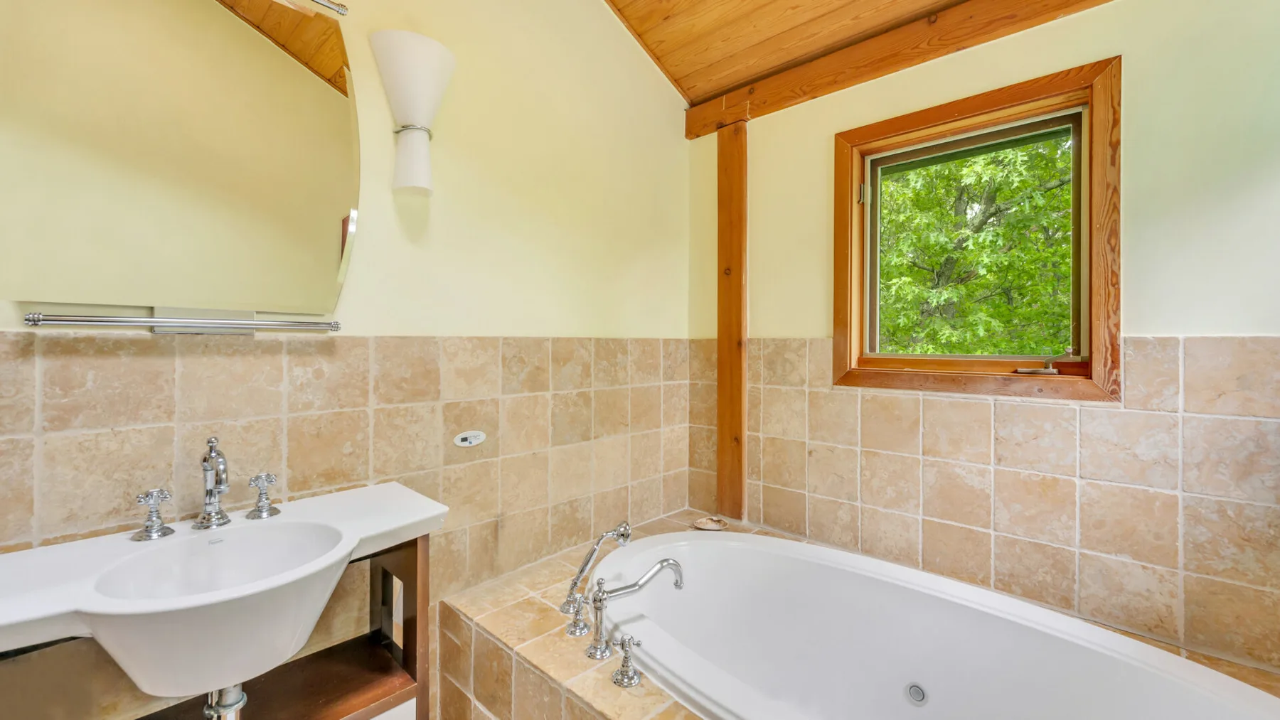 Un baño con bañera, lavabo y una ventana con vistas a la vegetación.