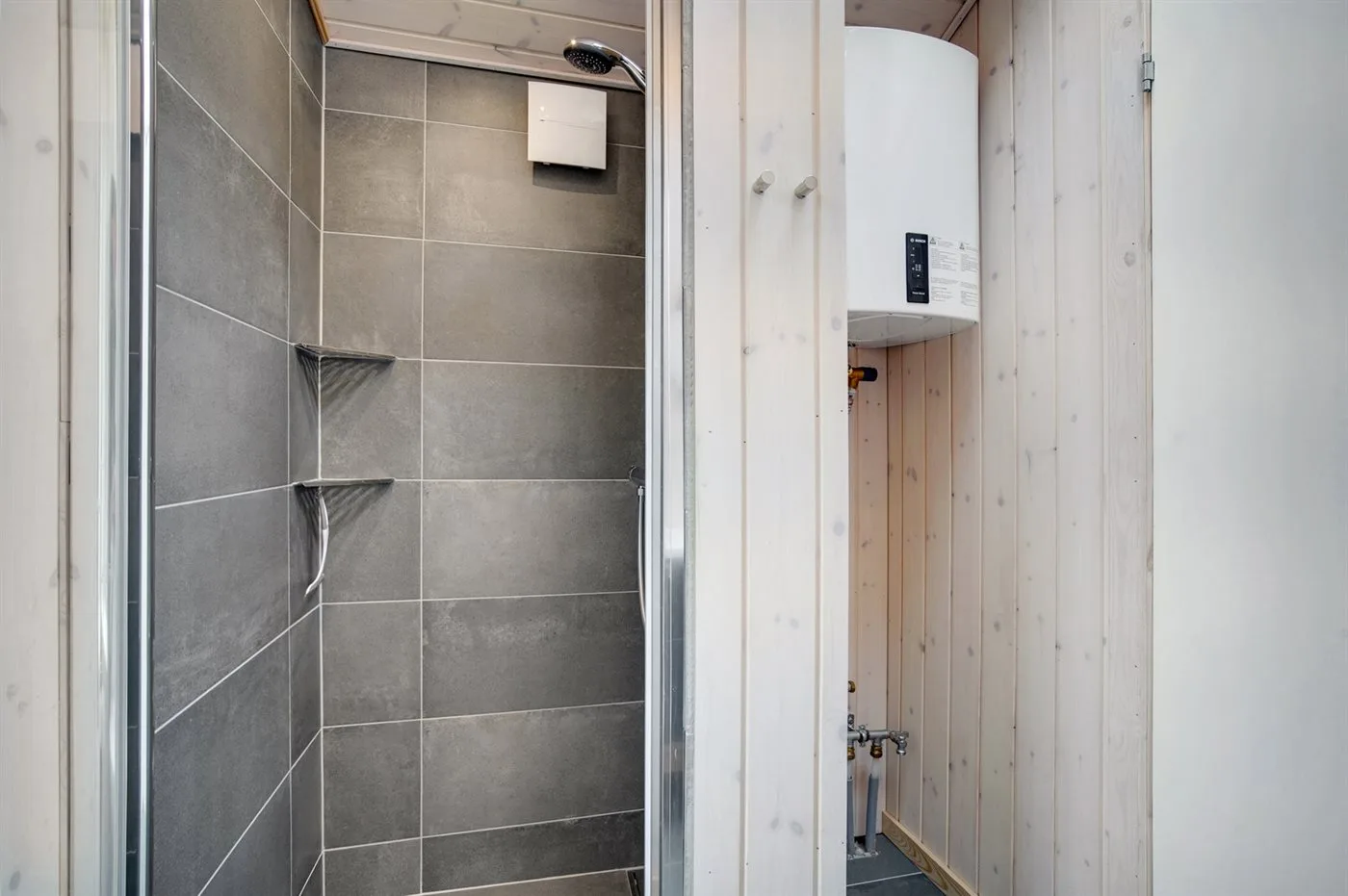 Una zona de ducha con azulejos junto a una pared revestida de madera.