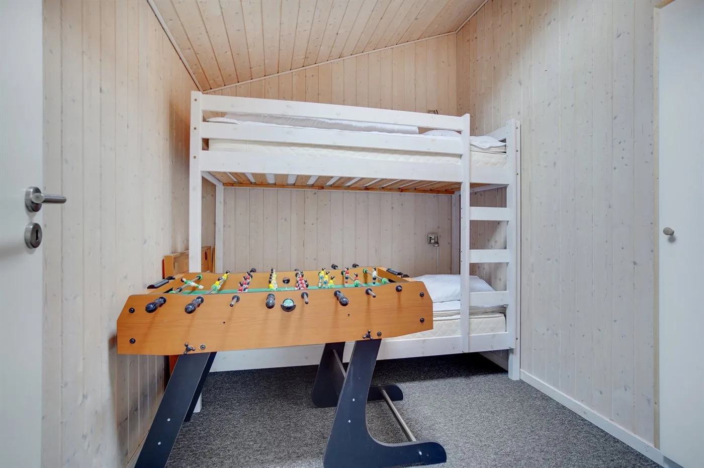 Una sala de juegos con un futbolín debajo de una litera.