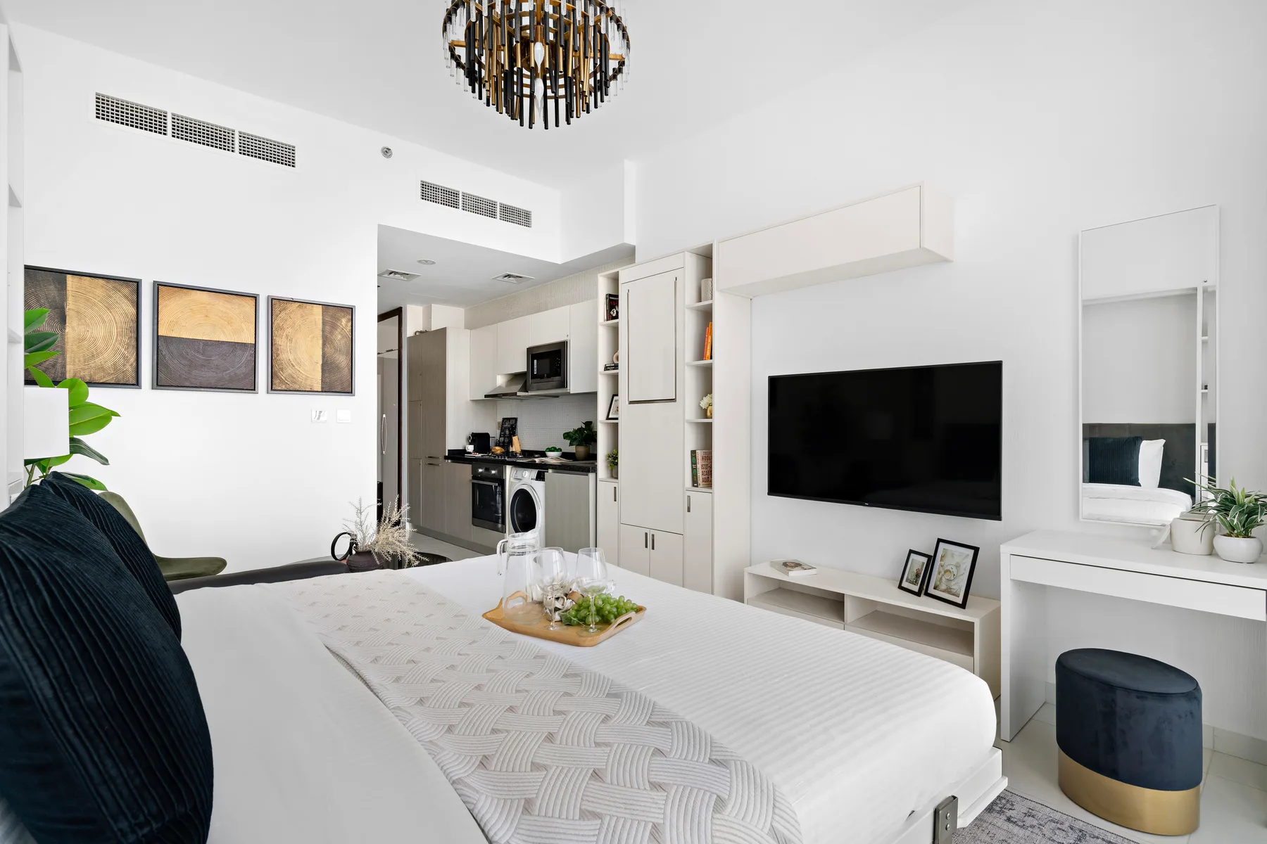 Un dormitorio luminoso con una cama grande, televisor de pared y zona de cocina.