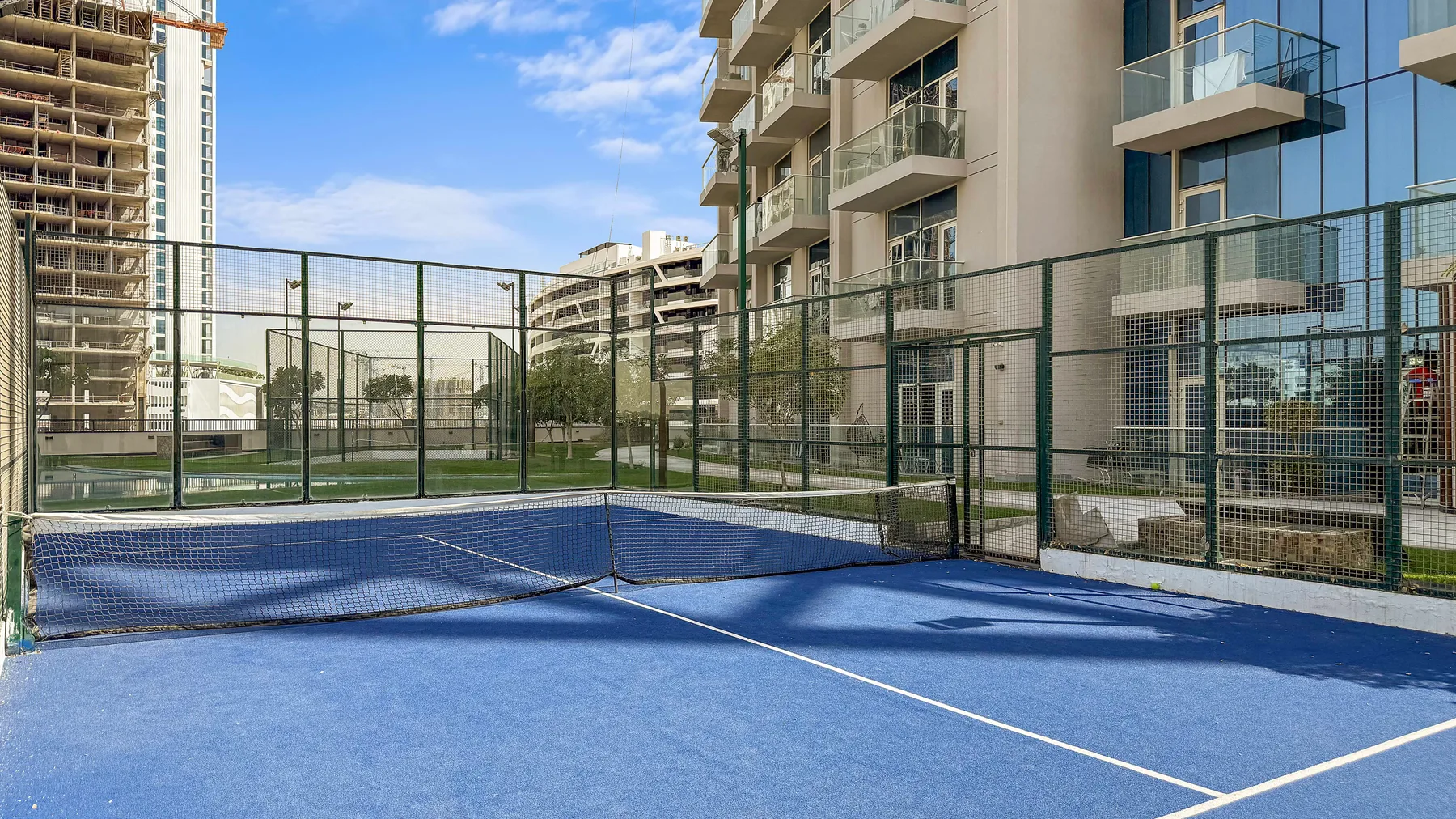 Una pista deportiva al aire libre con una red, rodeada de edificios de apartamentos modernos.