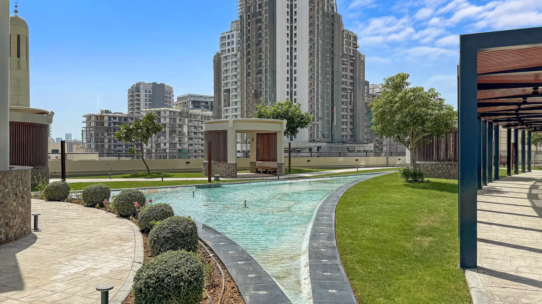 Un patio ajardinado cuenta con una piscina poco profunda, senderos curvos y edificios altos.