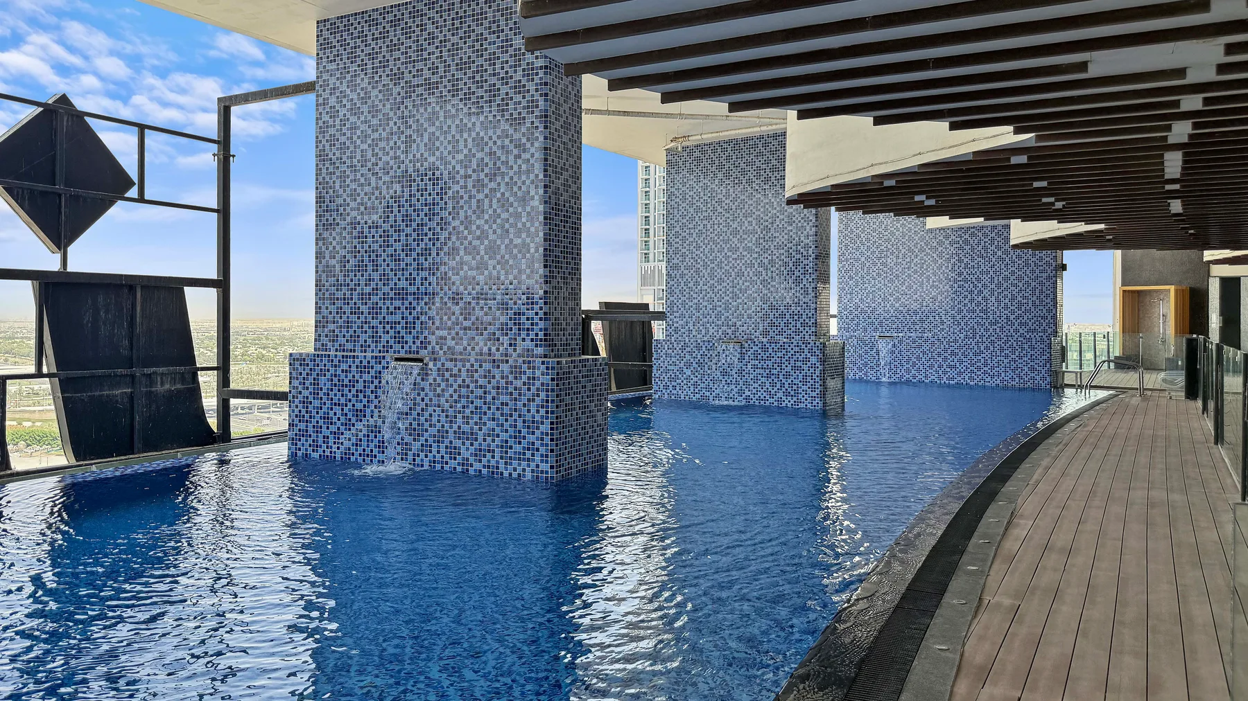 Una piscina azul bordea una terraza de madera bajo un techo sombreado.