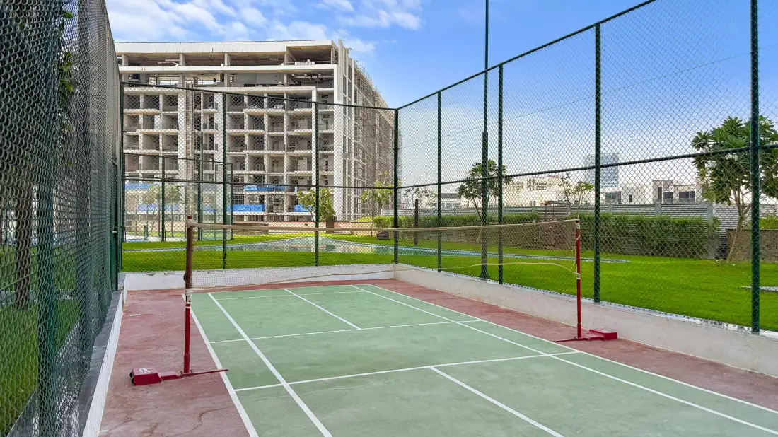 Una pista de tenis al aire libre está rodeada de vallas altas, con edificios al fondo.