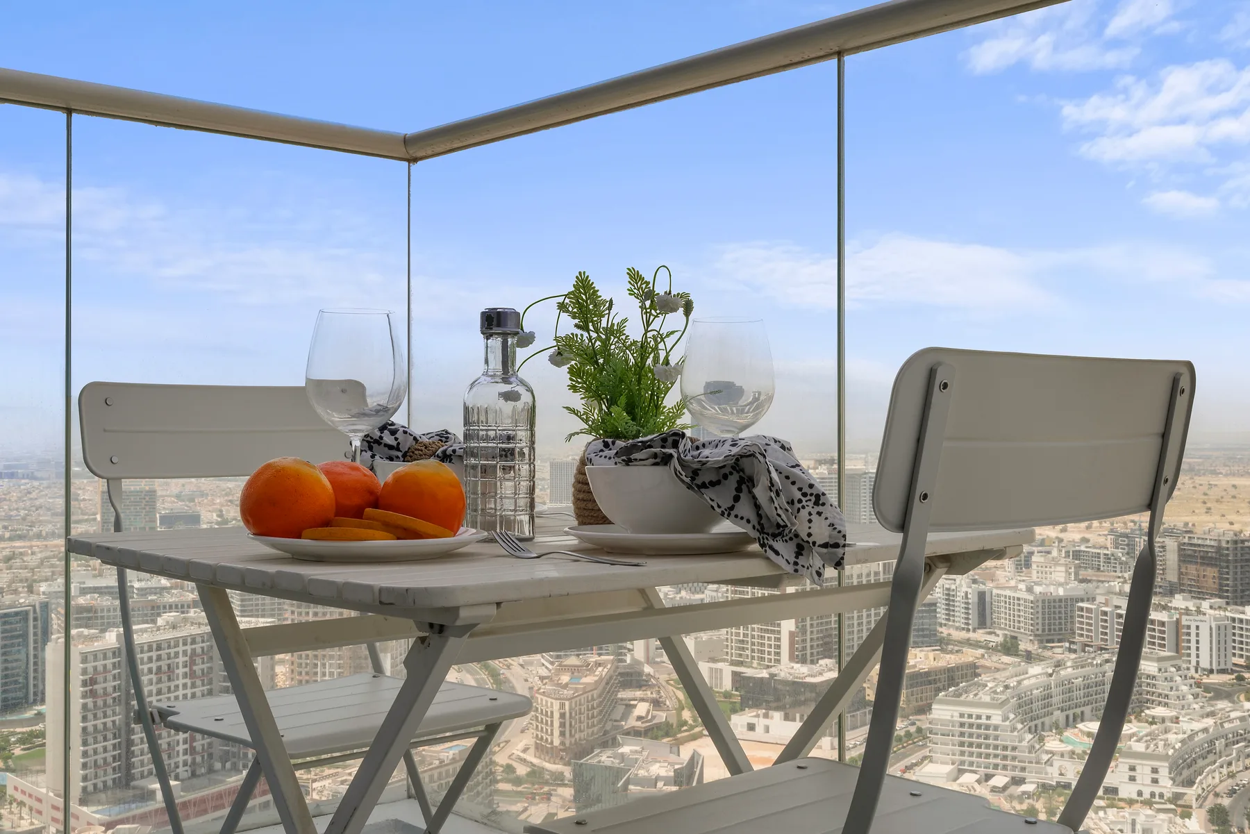 Una mesa y asientos en un balcón dan a un paisaje urbano.