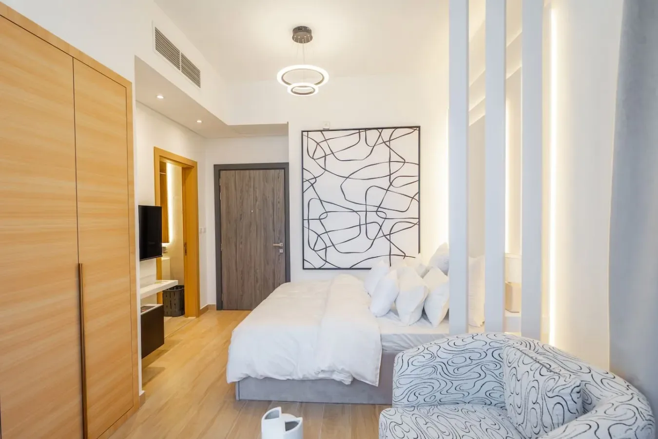 Un dormitorio luminoso con ropa de cama blanca y un cuadro abstracto sobre la cama.