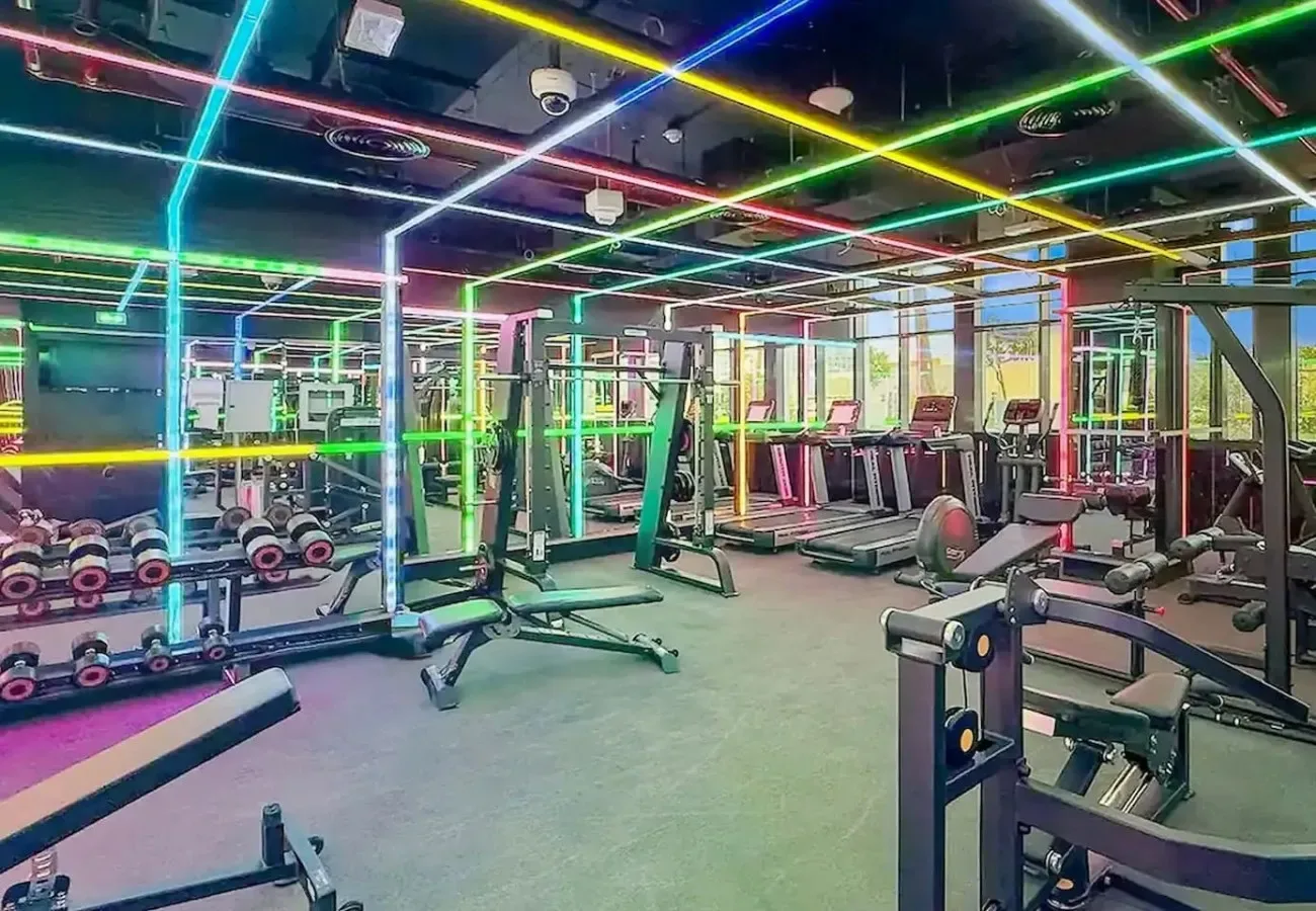 A gym with weight machines, free weights, and colorful lights across the ceiling.