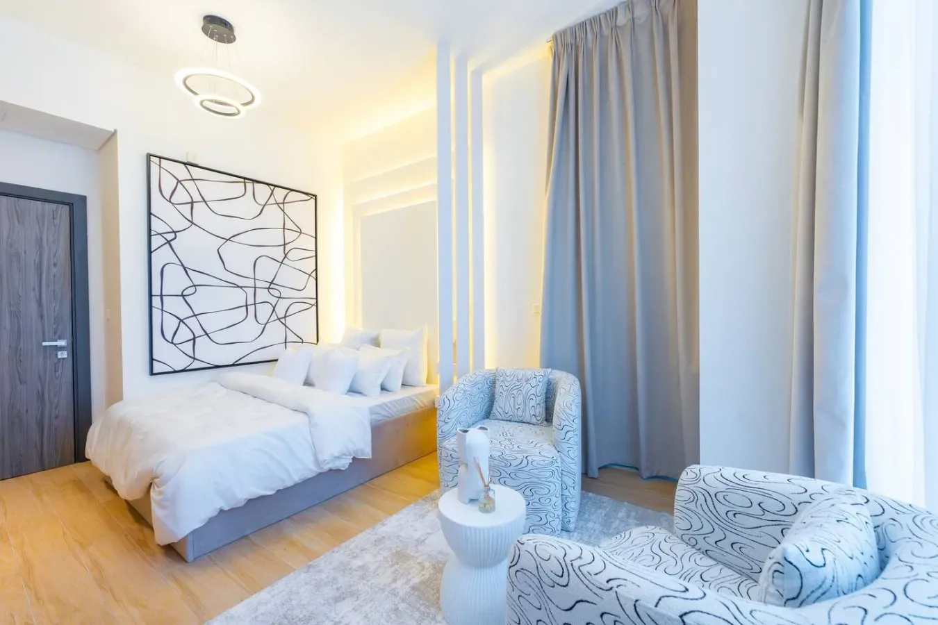 Un dormitorio luminoso con una cama, asientos estampados y cortinas.