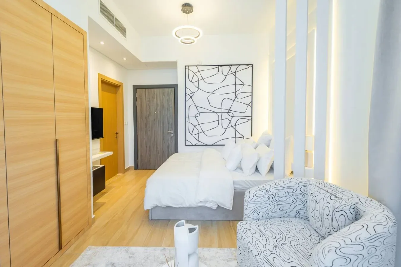 Un dormitorio luminoso con una cama, asientos estampados y arte abstracto en la pared.