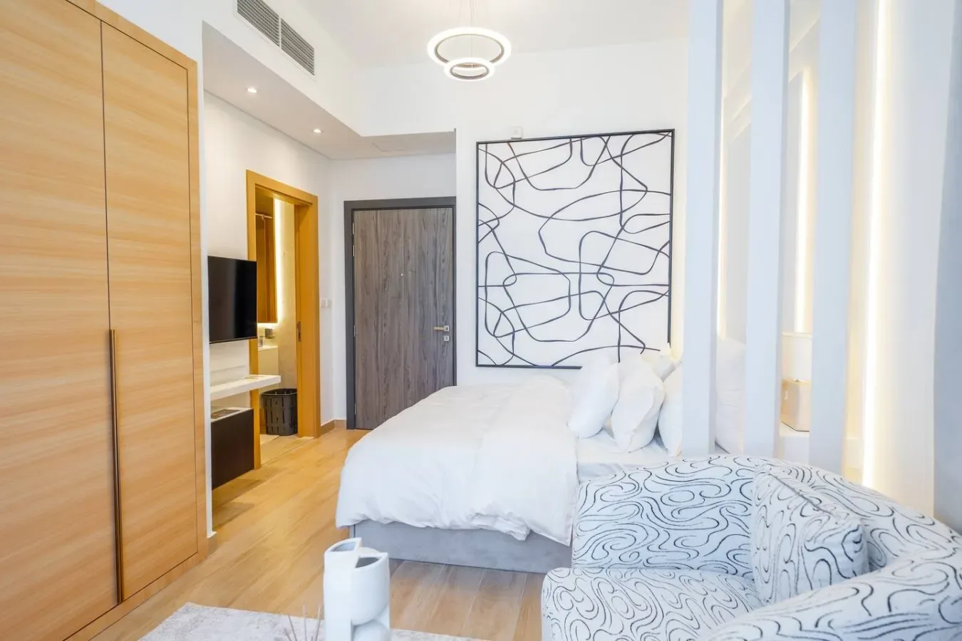 Un dormitorio con una cama, asientos estampados y arte abstracto en la pared.