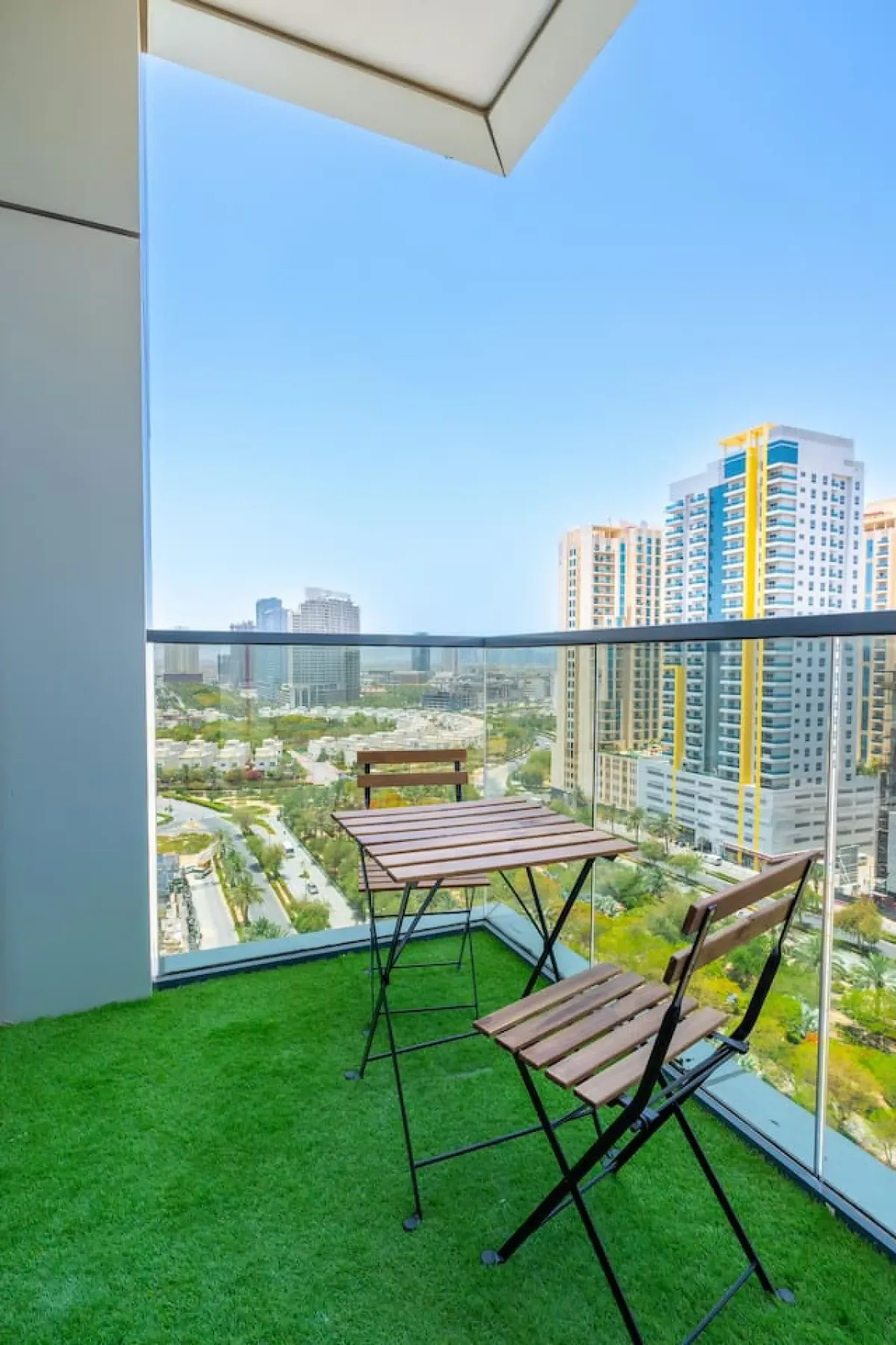 A balcony seating area overlooks nearby high-rise buildings and greenery.