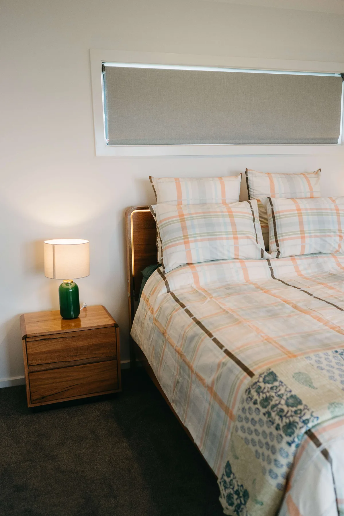 A bedroom with a bed dressed in plaid bedding and a bedside table.