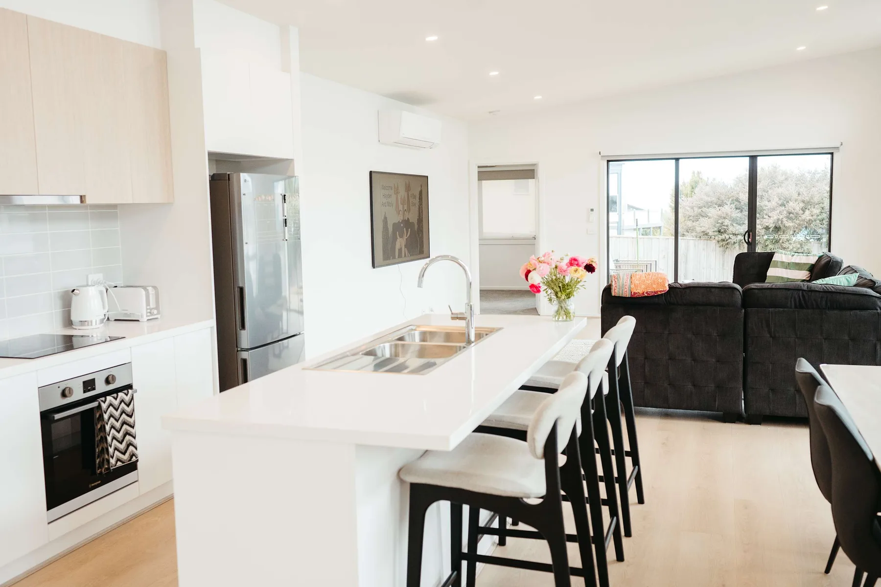 A bright open-plan kitchen and living area with a dining island and dark seating.