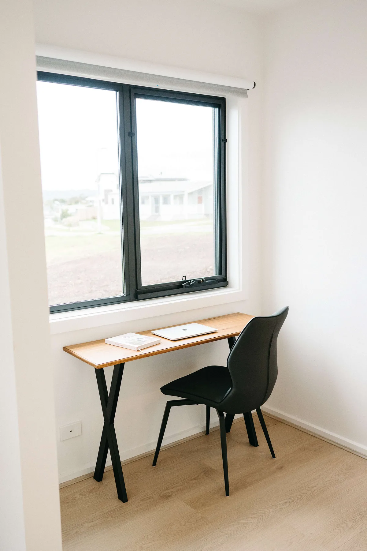 A small desk and chair sit beneath a window in a bright room.