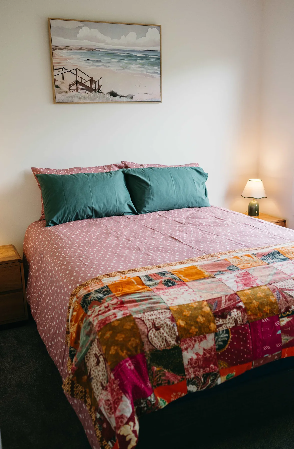 A bedroom with a bed dressed in pink bedding and teal pillows.